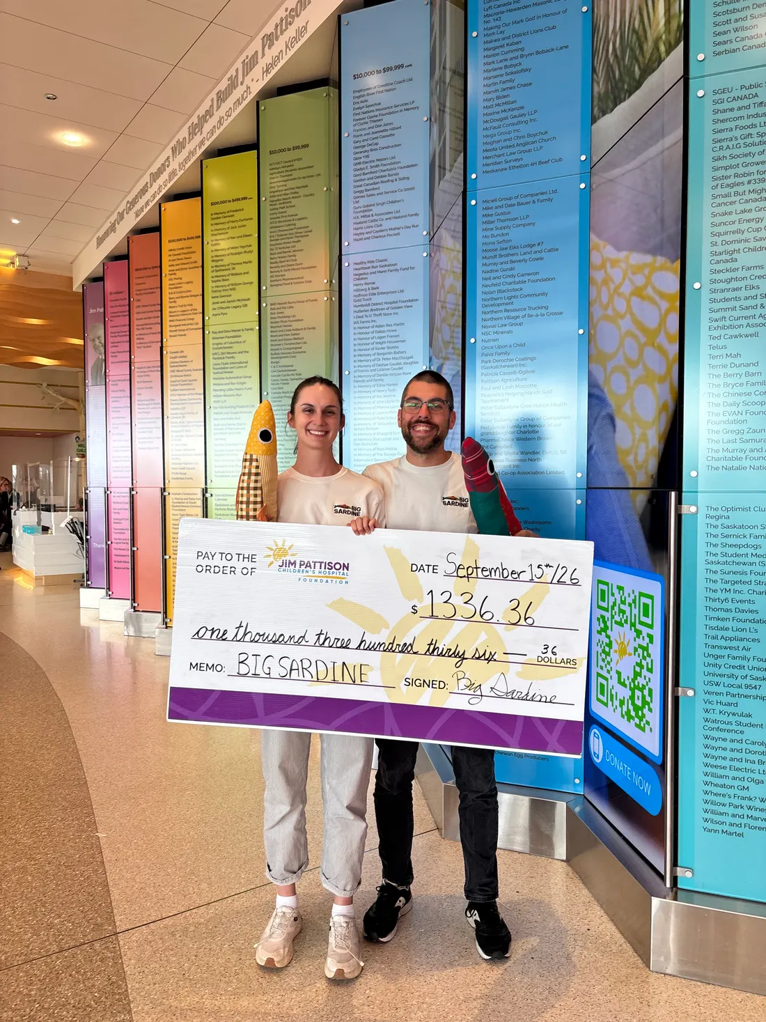 Two BIG SARDINE makers holding a giant cheque for $1,336.36 made out to the Jim Pattison Children's Hospital Foundation, each holding a plush sardine.